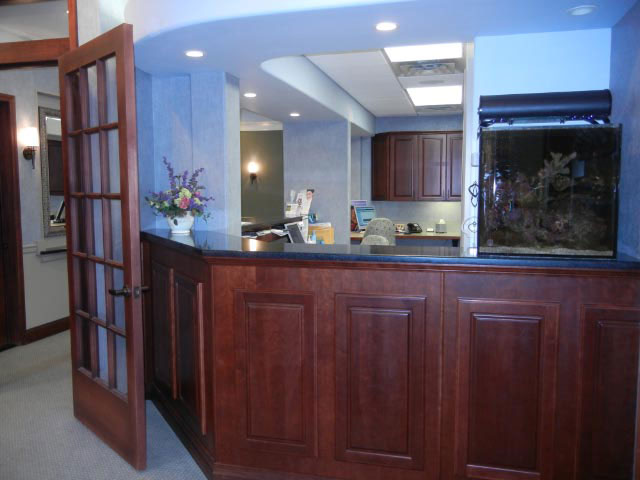 The image shows an interior view of a reception area with a counter, cabinetry, fish tank, and a person partially visible behind the counter.