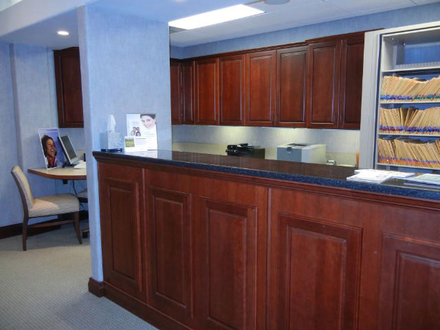 The image shows an interior view of a spacious office area with a reception desk and counter, featuring dark wood cabinetry, a black countertop, and a well-lit space.