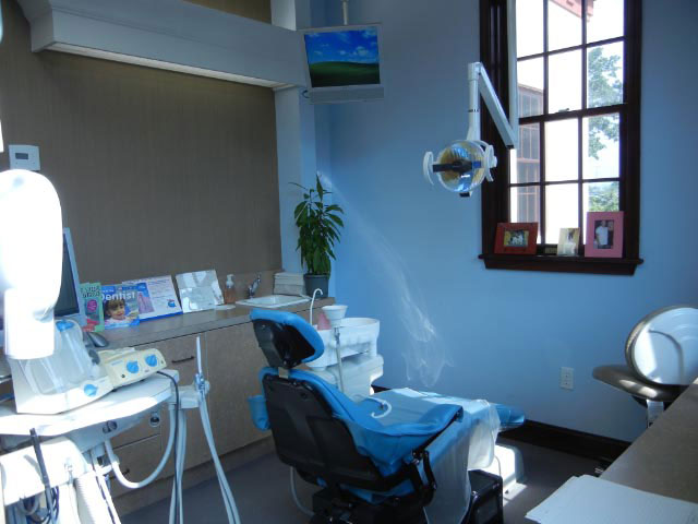 The image shows a dental office interior with a dentist s chair and equipment, a window with sunlight streaming through, and a blue wall.