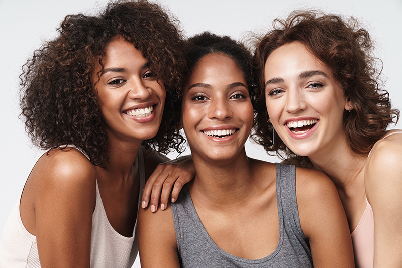 Three women smiling at the camera with one arm around another.