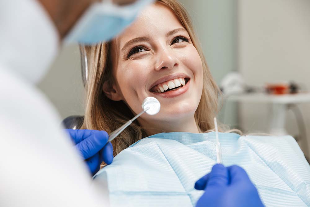 A dental hygienist is smiling at a patient who is seated in a dentist s chair, receiving dental care.