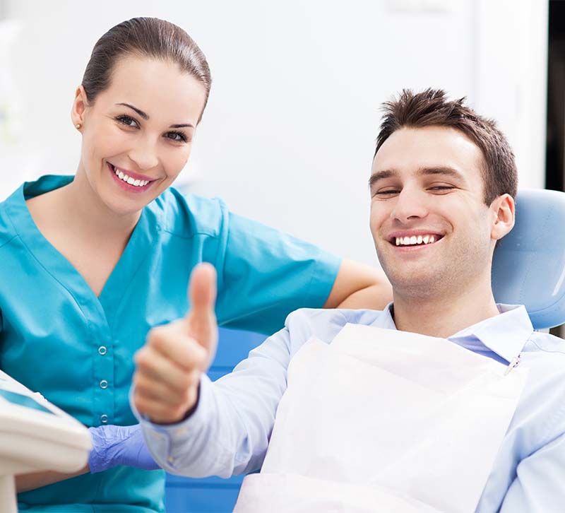 A dental professional and patient are smiling at the camera, with the dentist giving a thumbs-up gesture.