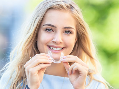 A young woman holding up a clear dental retainer with a smile on her face.