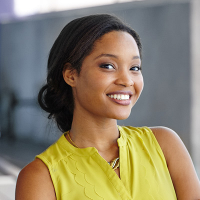 A woman with a smile, wearing a yellow top, poses against a blurred background.